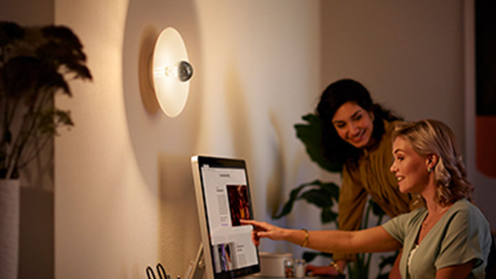 Frauen, die neben einer Philips LED-Spiegelwandlampe am Computer arbeiten.