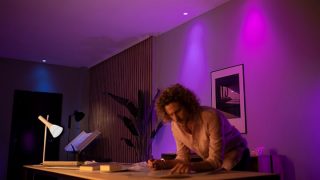Les lampes LED connectées Philips Hue créent une ambiance violette et rose vibrante dans le salon, présentant un éclairage d'ambiance personnalisable pour les soirées cinéma et la détente dans les maisons modernes.