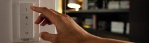 "Main ajustant l'interrupteur variateur LED connecté Philips, qui contrôle l'éclairage ambiant dans un salon confortable avec étagères."