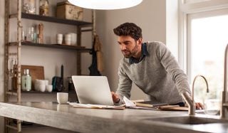 Un homme utilise un ordinateur portable dans un bureau à domicile bien éclairé avec un éclairage de travail à LED pour une configuration de travail à distance efficace.