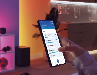 "Une femme contrôle l'éclairage LED connecté via une application pour smartphone, ajustant la lueur ambiante rose pour une atmosphère personnalisée."